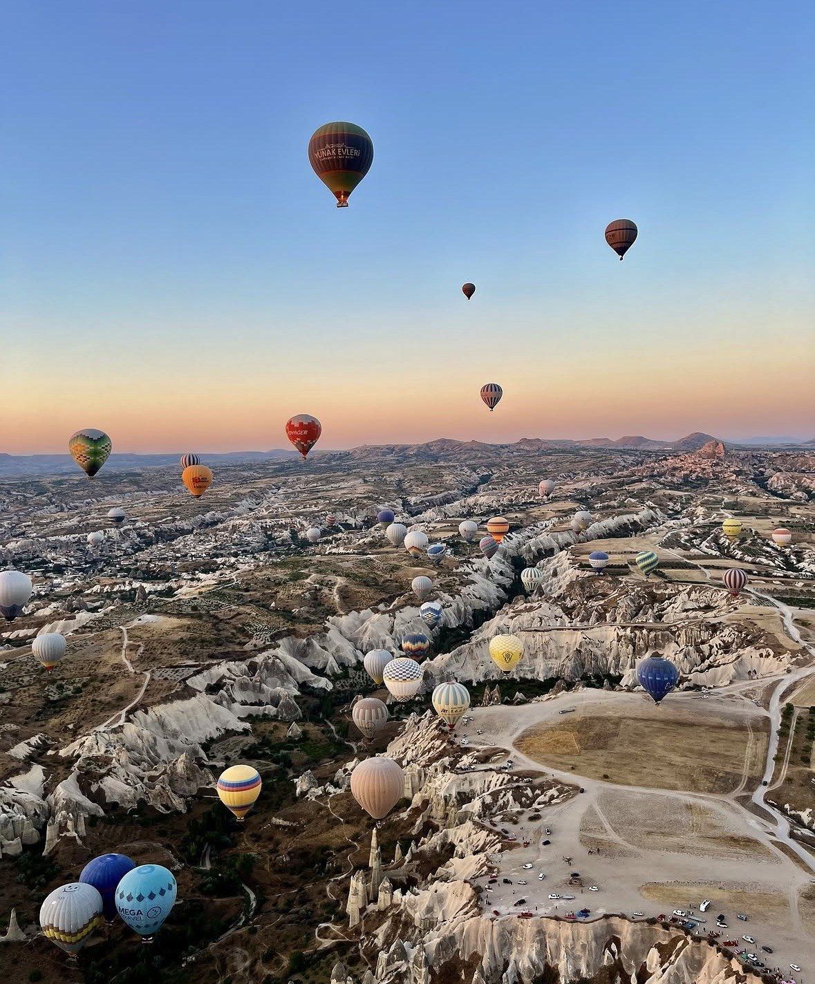 Aerial view of Cappadocia rock valleys with balloons spread to horizon