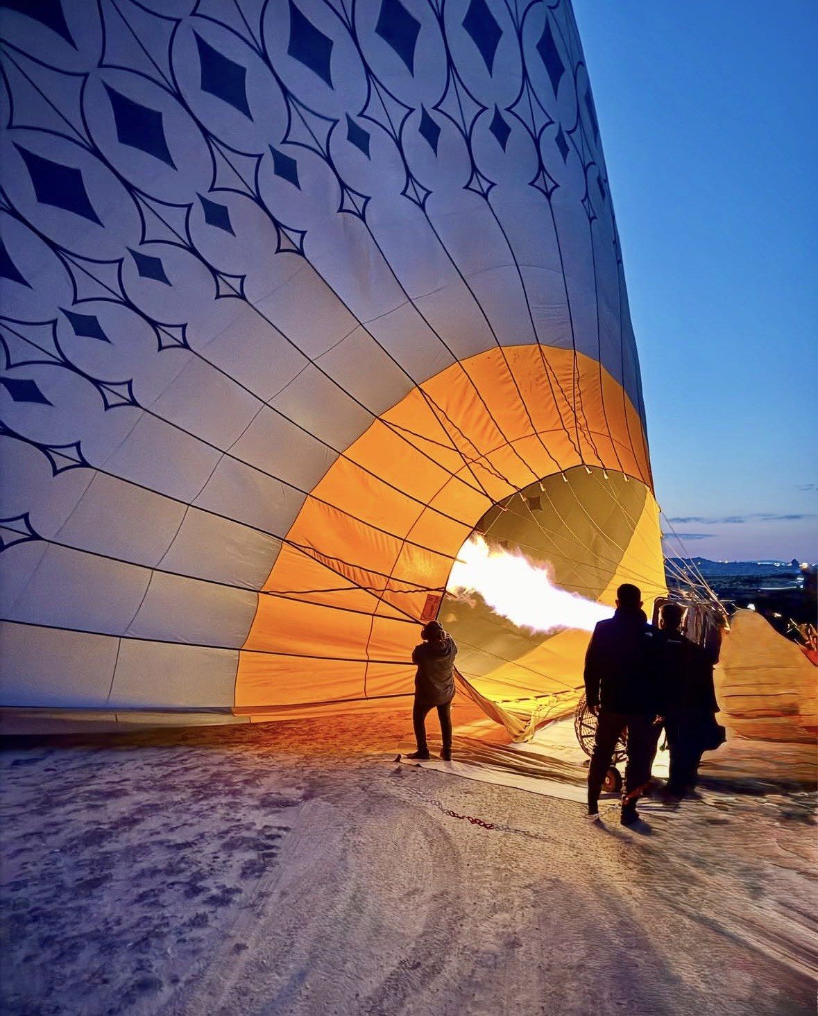 Crew inflating a balloon envelope with burner flame before dawn in Cappadocia