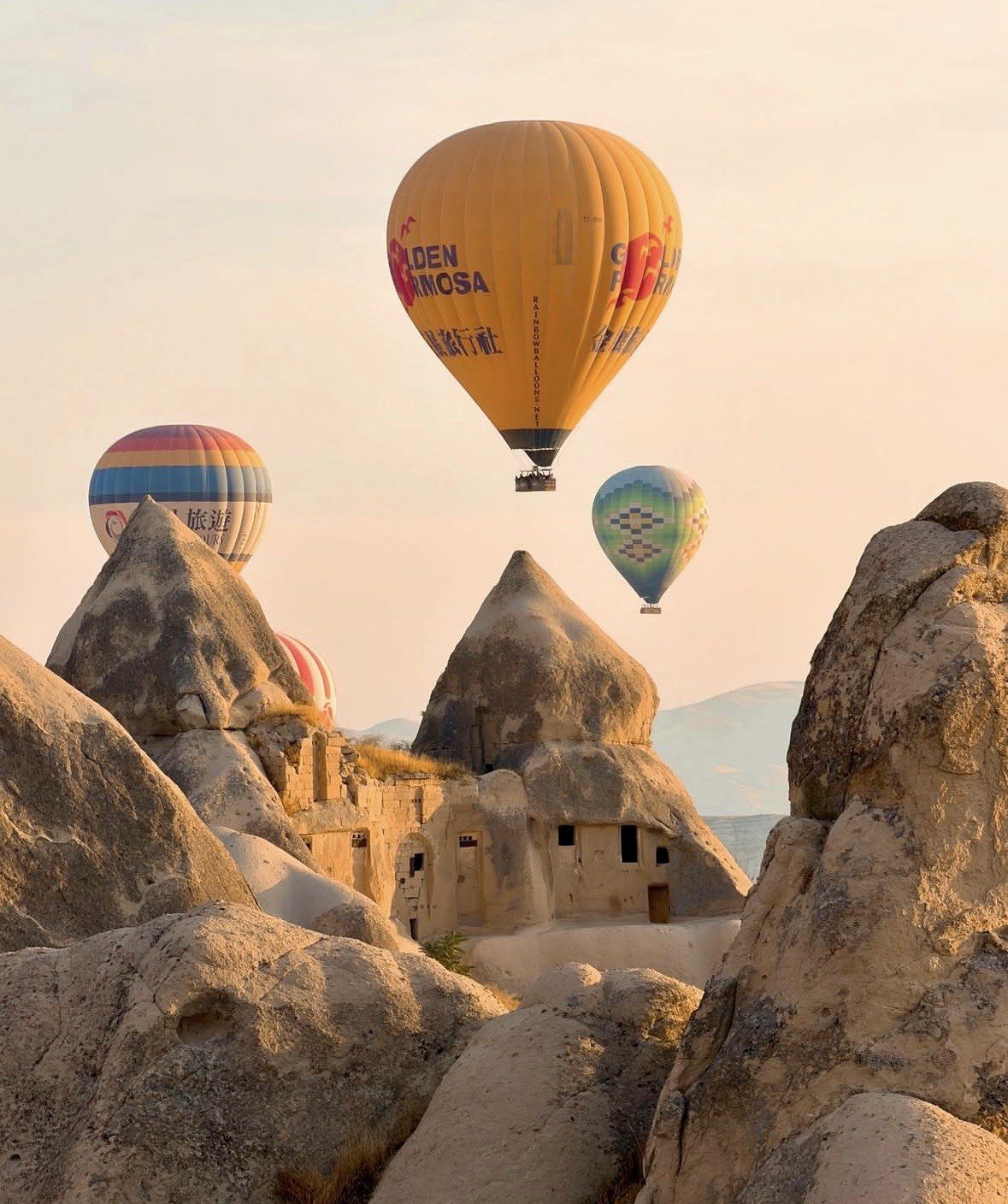 Balloons above carved cave dwellings and fairy chimneys in Cappadocia tuff rock