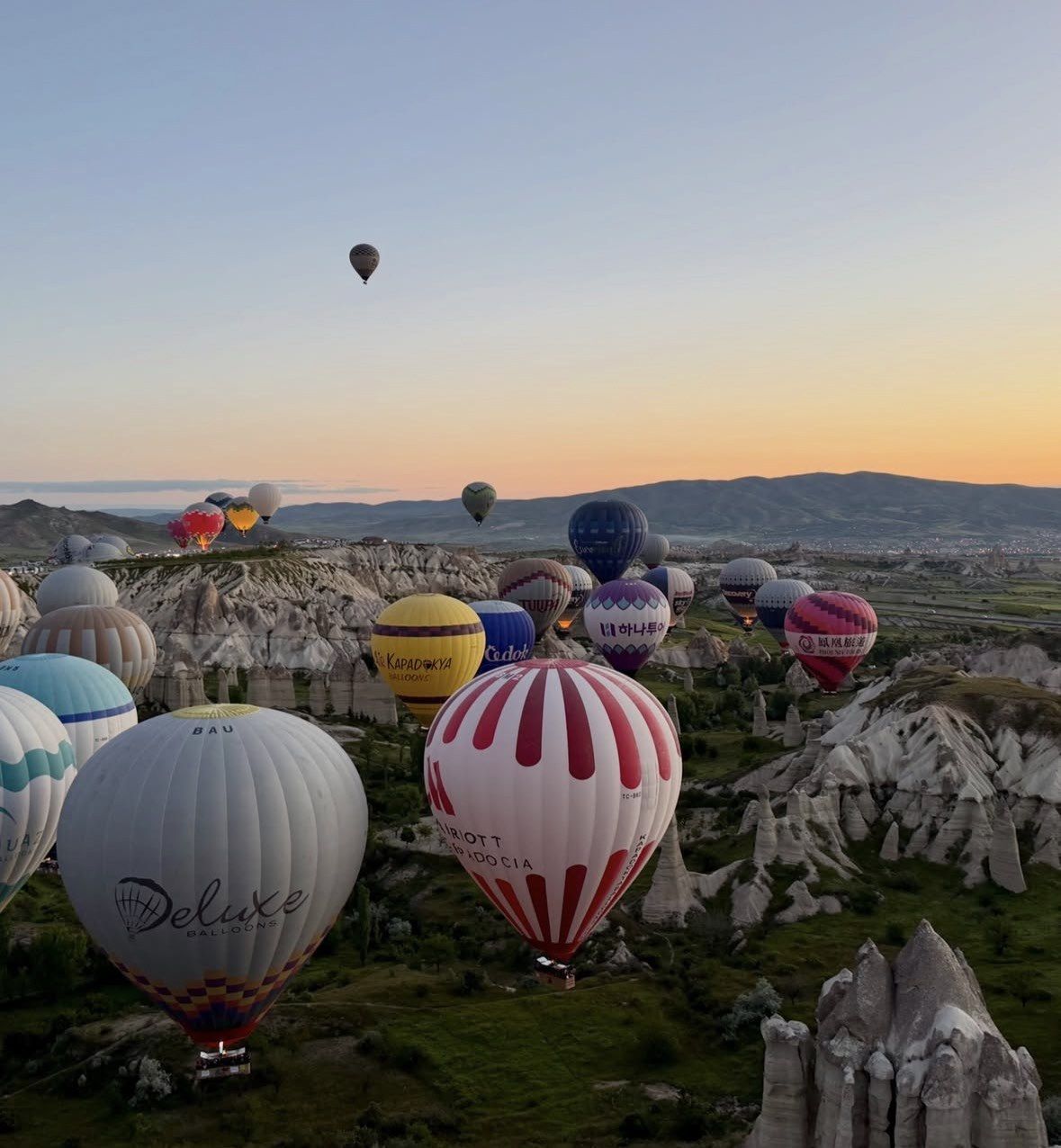 Dozens of colorful balloons lifting off together from Cappadocia valley floor