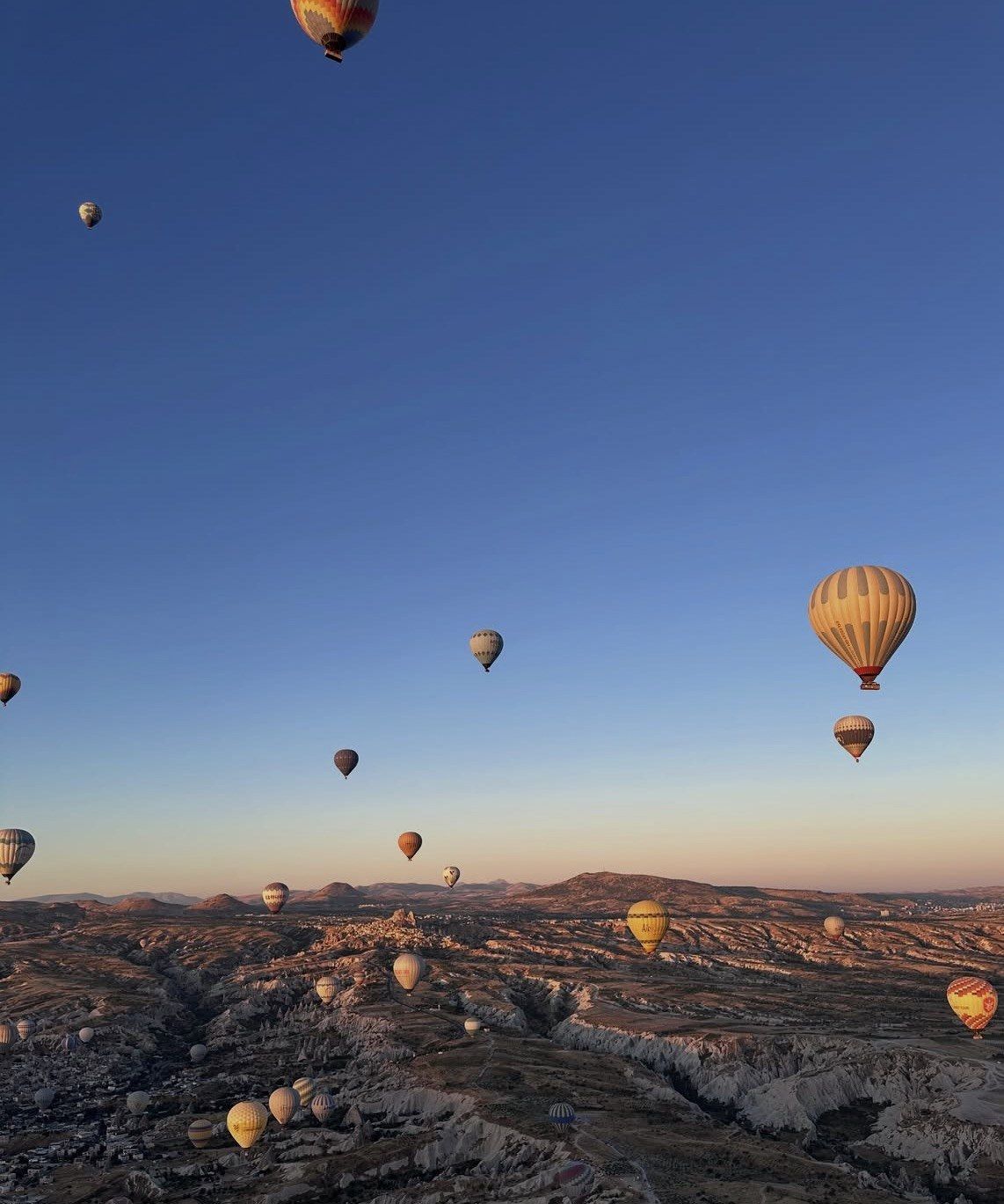 Balloons climbing into deep blue sky above Cappadocia's pale rock plateau