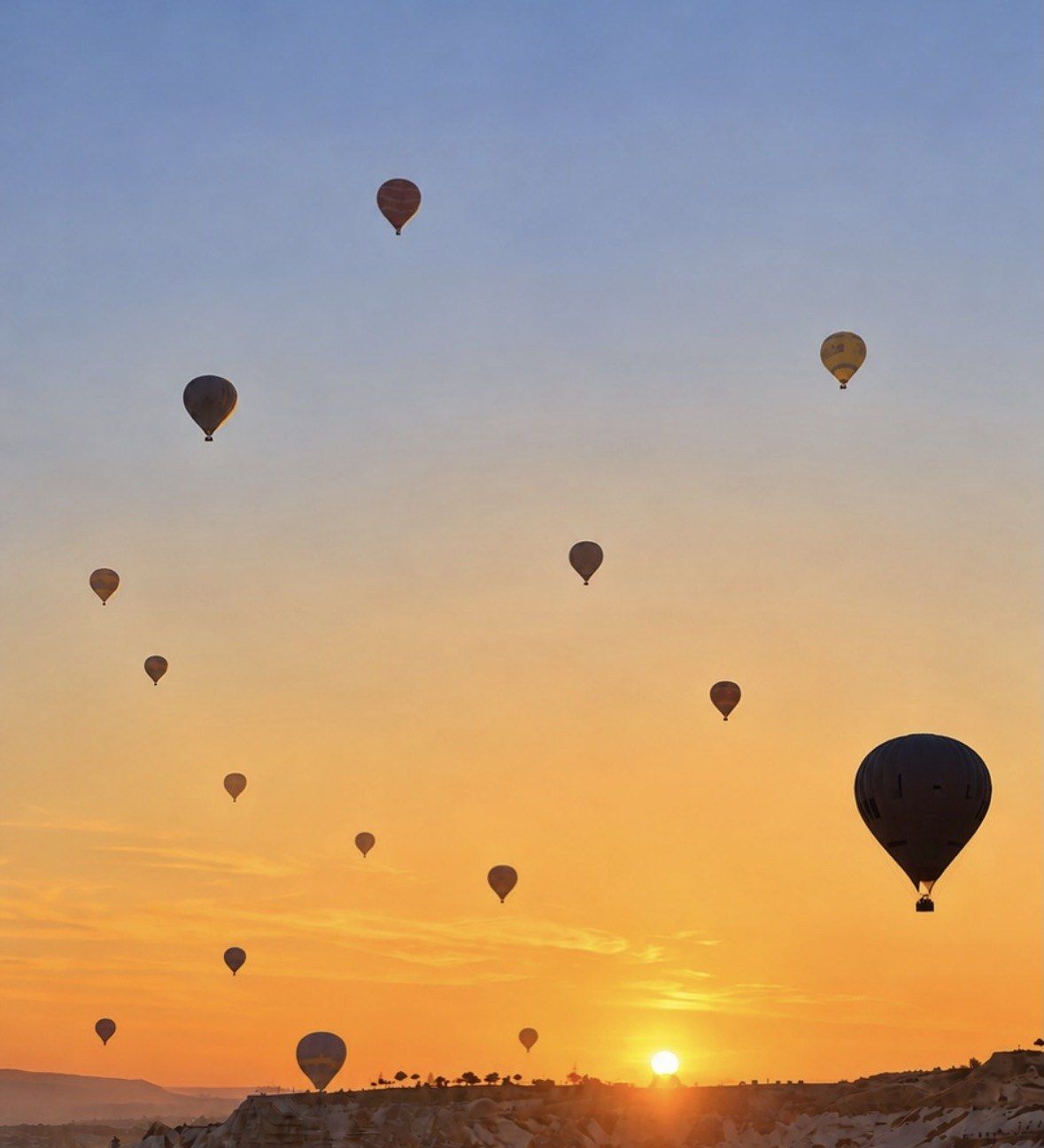 Scattered balloons drifting in golden and blue sky above Cappadocia at sunrise