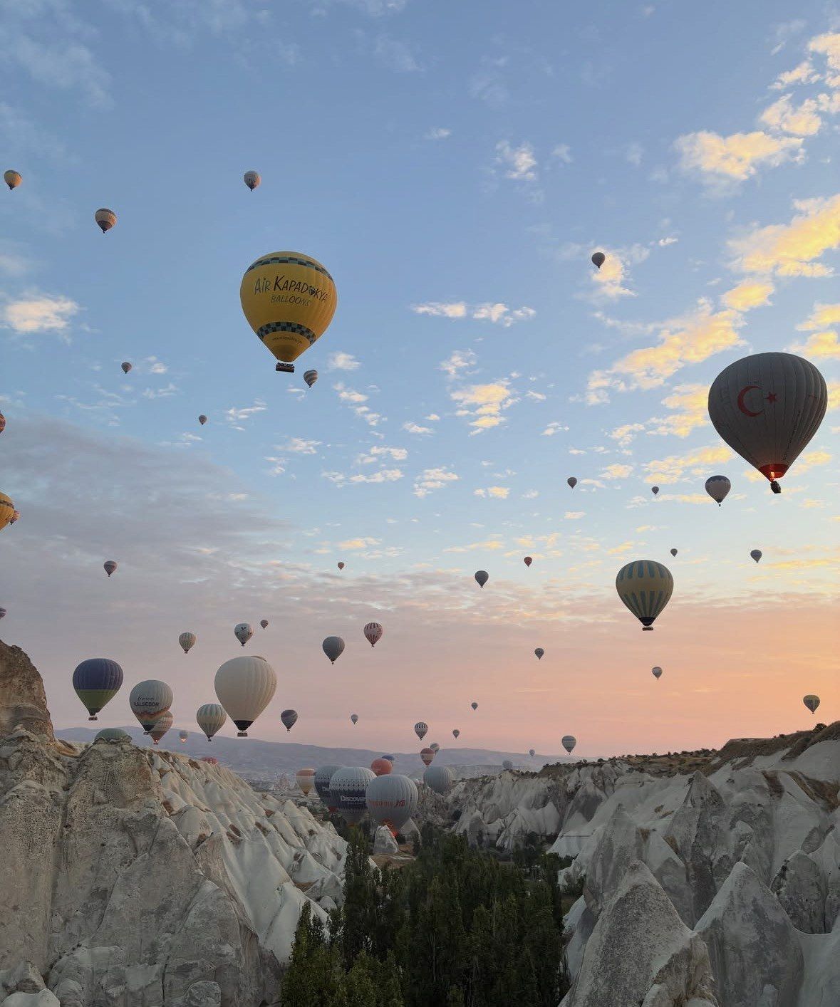 Balloons rising from white Cappadocia canyon into soft pastel morning sky