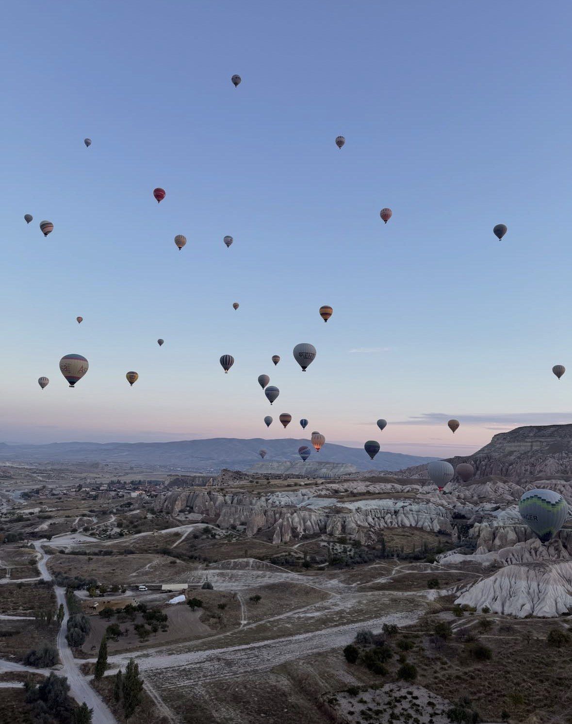Wide twilight panorama of Cappadocia valley with balloons above winding roads